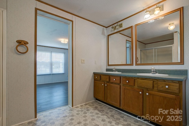 bathroom with double vanity, a sink, a shower with door, and ornamental molding