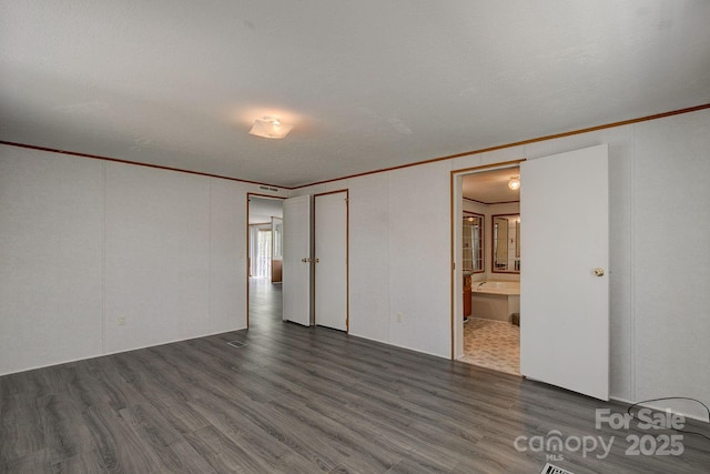 unfurnished bedroom featuring ensuite bathroom, ornamental molding, and wood finished floors