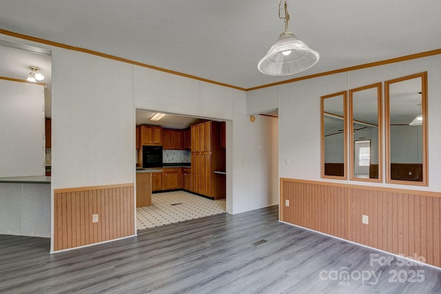 unfurnished living room with visible vents, crown molding, wainscoting, wood walls, and wood finished floors