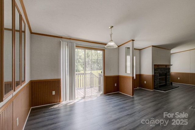 unfurnished living room with ornamental molding, wainscoting, wood walls, wood finished floors, and a stone fireplace