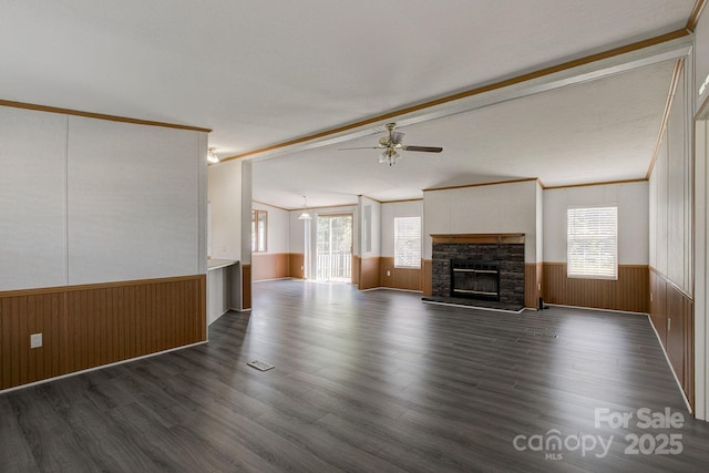 unfurnished living room with ceiling fan, a stone fireplace, wainscoting, dark wood-style floors, and vaulted ceiling with beams
