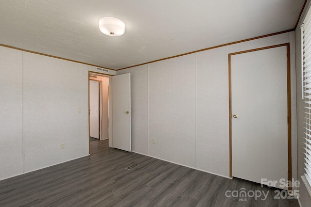 unfurnished room with dark wood-style flooring, visible vents, and ornamental molding