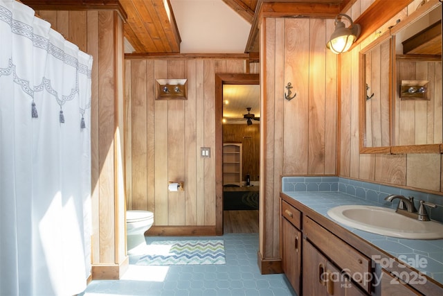 full bathroom featuring wooden walls, vanity, toilet, tile patterned floors, and a ceiling fan