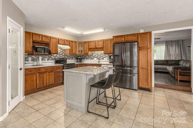 804 Rostan St SE, Valdese, NC 28690 - kitchen featuring stainless steel appliances, under cabinet range hood, tasteful backsplash, light tile patterned floors, and glass insert cabinets
