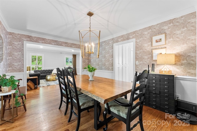 dining area with crown molding, light wood-style floors, wallpapered walls, a wainscoted wall, and a notable chandelier