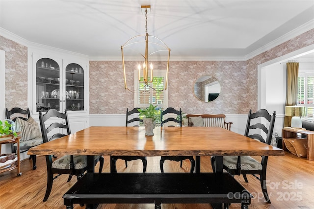dining area with ornamental molding, a wainscoted wall, a chandelier, and wallpapered walls