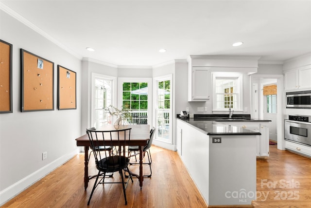 kitchen with dark countertops, a sink, light wood finished floors, stainless steel appliances, and a peninsula