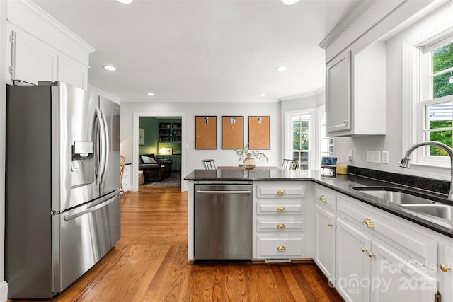 kitchen with appliances with stainless steel finishes, a sink, white cabinets, a peninsula, and ornamental molding
