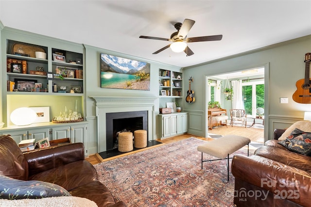 living area with crown molding, a ceiling fan, built in shelves, and light wood-type flooring