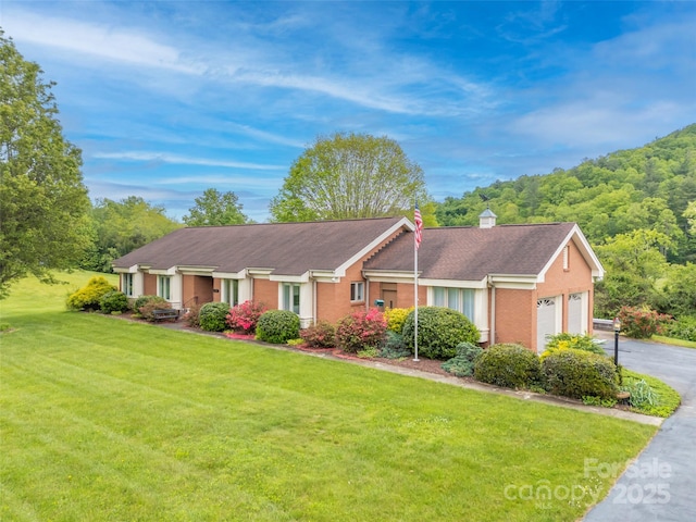 single story home featuring a front yard, a chimney, an attached garage, and roof with shingles