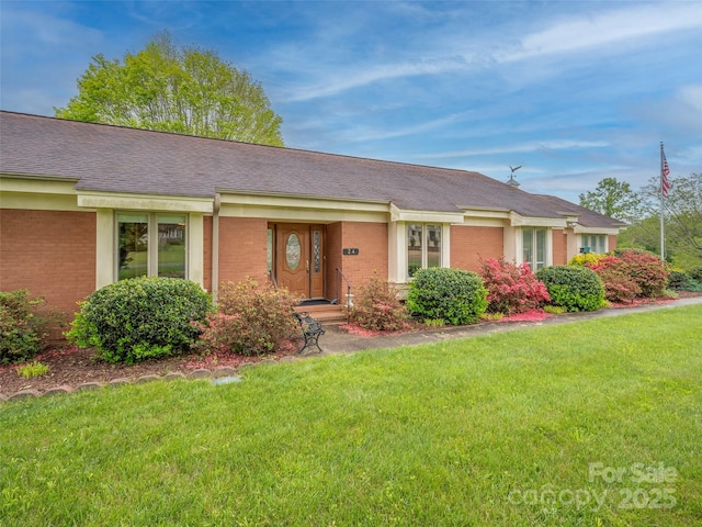 view of front of property featuring brick siding, a front lawn, and a shingled roof