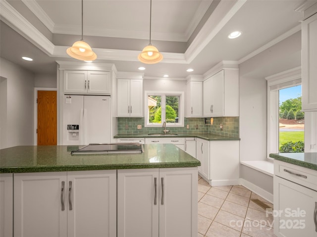 kitchen with a sink, white refrigerator with ice dispenser, stovetop, a tray ceiling, and ornamental molding