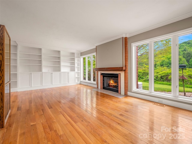 unfurnished living room with light wood finished floors, a fireplace with flush hearth, healthy amount of natural light, ornamental molding, and built in features