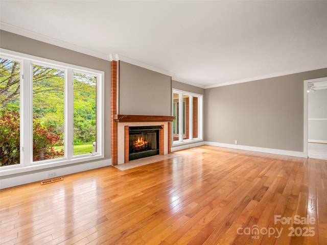 unfurnished living room featuring a fireplace, light wood finished floors, crown molding, and baseboards