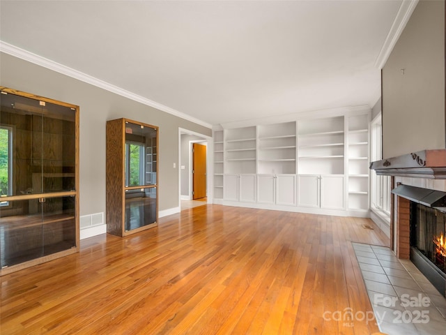 unfurnished living room featuring a tile fireplace, wood-type flooring, ornamental molding, baseboards, and built in shelves