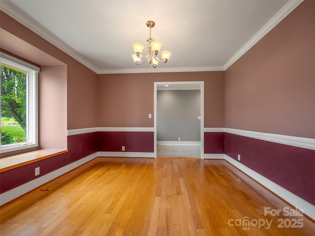 empty room with a chandelier, light wood-style flooring, baseboards, and crown molding