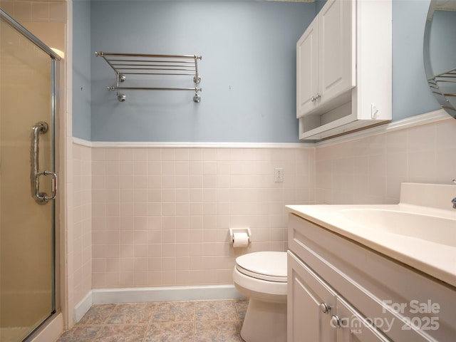 bathroom with a shower stall, tile walls, vanity, toilet, and a wainscoted wall