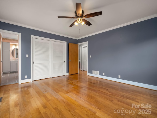 unfurnished bedroom with baseboards, crown molding, light wood-style floors, ensuite bathroom, and a closet