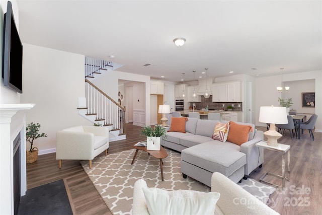 living room with stairs, light wood-style floors, baseboards, a chandelier, and a fireplace