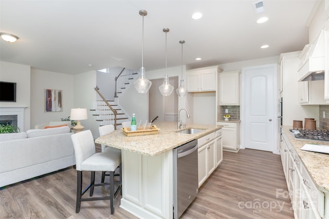 kitchen with appliances with stainless steel finishes, a sink, open floor plan, tasteful backsplash, and light wood-style flooring