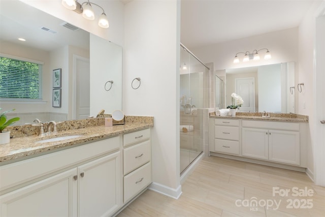 full bathroom featuring a shower stall, two vanities, and baseboards