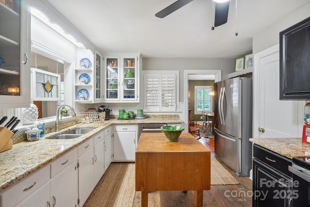 kitchen with freestanding refrigerator, a ceiling fan, a sink, white cabinetry, and wood finished floors