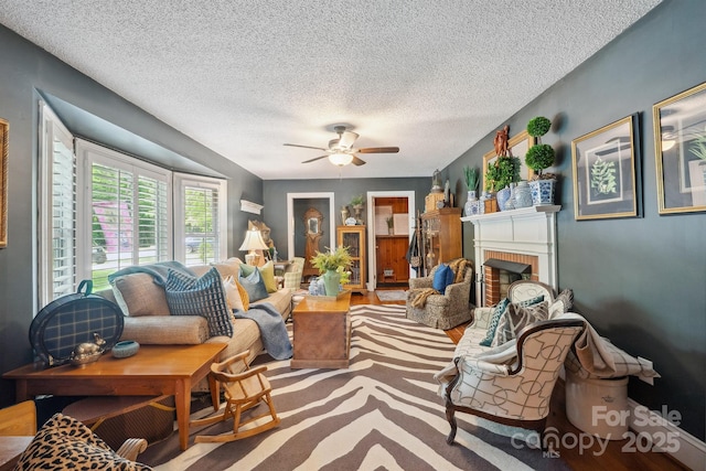 living area featuring a fireplace, a textured ceiling, and a ceiling fan