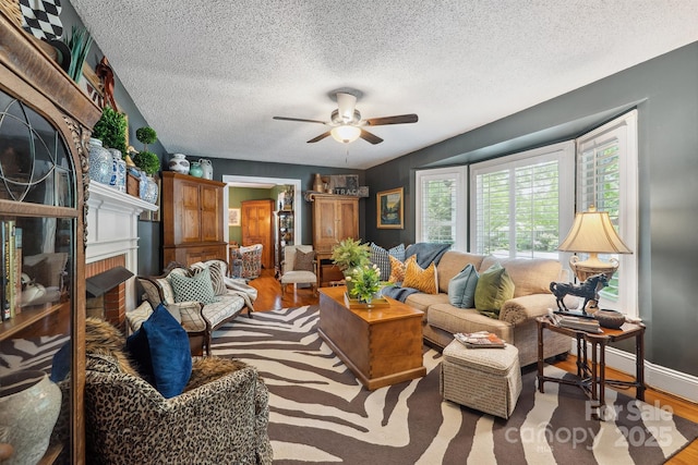 living area with wood finished floors, a ceiling fan, a brick fireplace, a textured ceiling, and baseboards