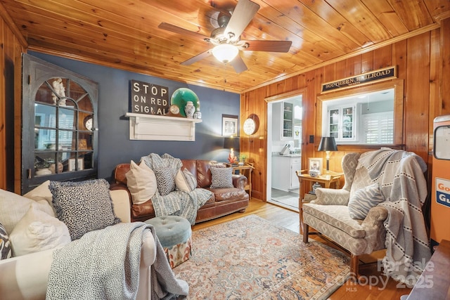 living room featuring wood finished floors, wooden ceiling, crown molding, wooden walls, and ceiling fan