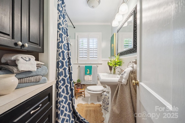 bathroom with toilet, a sink, a wainscoted wall, tile patterned floors, and crown molding