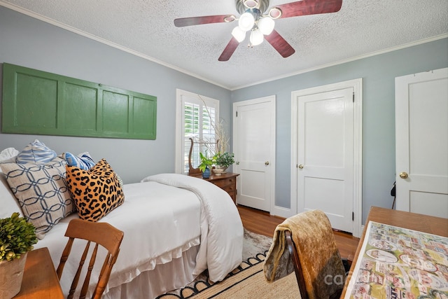 bedroom featuring a ceiling fan, a textured ceiling, two closets, crown molding, and wood finished floors