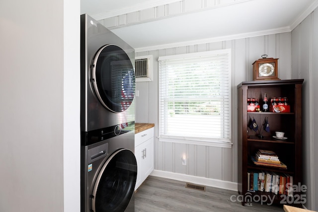 laundry area featuring visible vents, stacked washer / drying machine, cabinet space, baseboards, and light wood-style flooring
