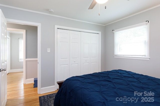 bedroom featuring ceiling fan, light wood-style floors, baseboards, ornamental molding, and a closet