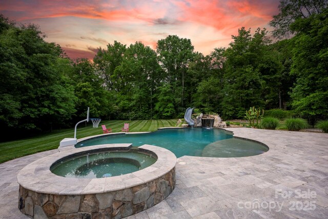 pool at dusk with a pool with connected hot tub, a water slide, a yard, and a patio area