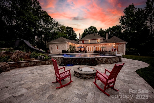 patio terrace at dusk featuring an outdoor pool and an outdoor fire pit