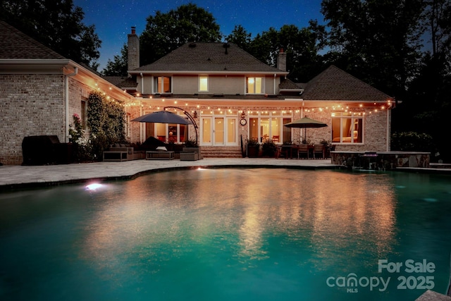 back of house at twilight with brick siding, a chimney, an outdoor hangout area, and a patio area