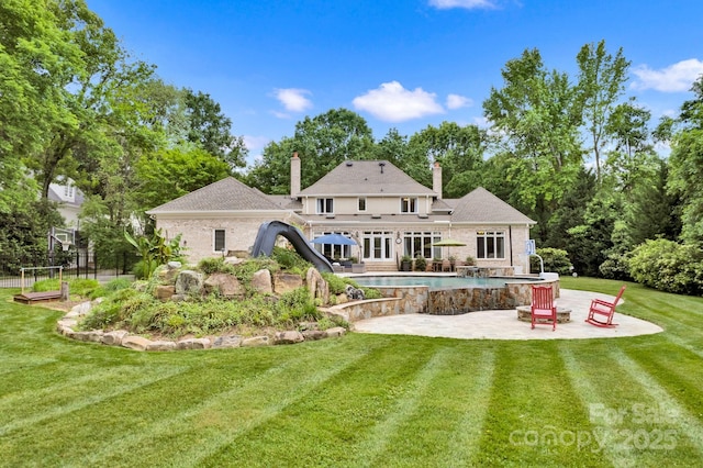 back of house featuring fence, a patio, an outdoor pool, a chimney, and a lawn