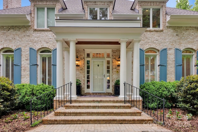 entrance to property featuring a shingled roof and brick siding