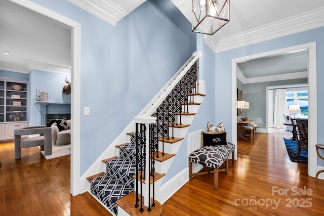 stairway featuring crown molding, a premium fireplace, baseboards, and wood finished floors