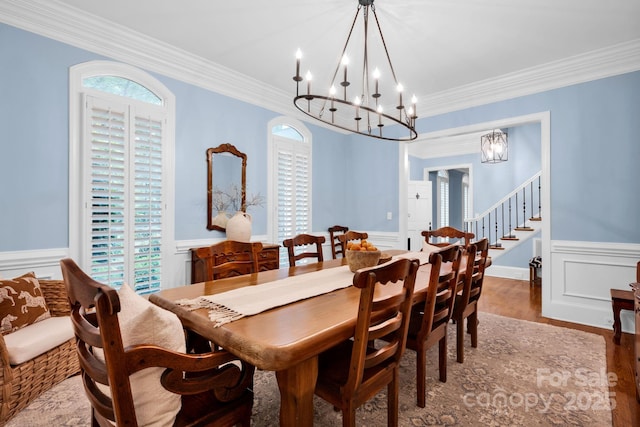 dining area featuring wainscoting, a decorative wall, a chandelier, stairs, and ornamental molding