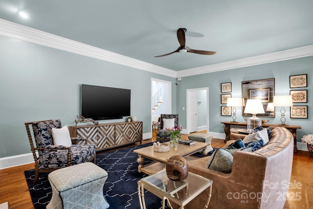 living area with crown molding, a ceiling fan, stairs, and wood finished floors