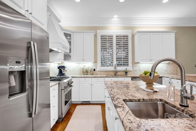 kitchen with a sink, appliances with stainless steel finishes, custom range hood, and white cabinetry