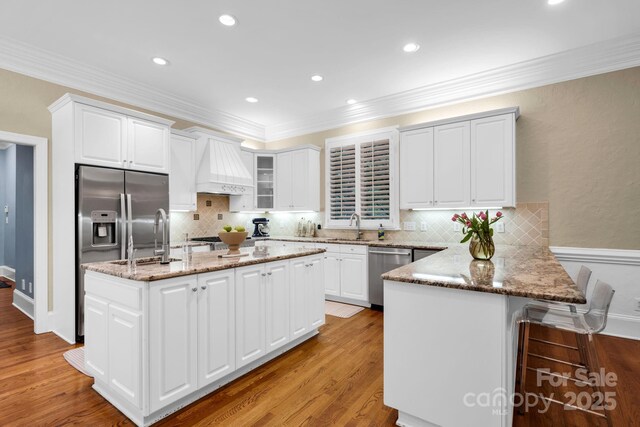 kitchen with appliances with stainless steel finishes, light stone countertops, premium range hood, a peninsula, and white cabinetry