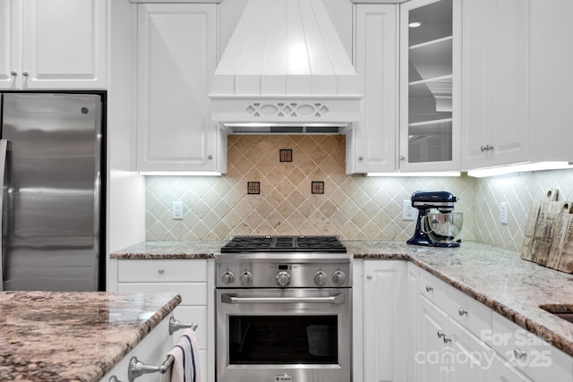 kitchen featuring glass insert cabinets, stainless steel appliances, white cabinetry, and custom range hood