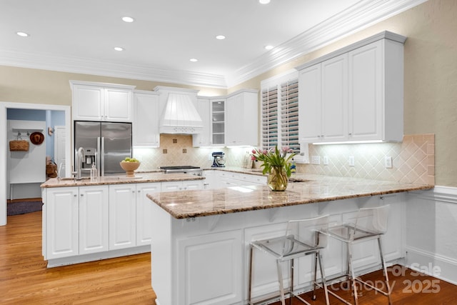 kitchen with white cabinets, stainless steel appliances, custom range hood, and a peninsula