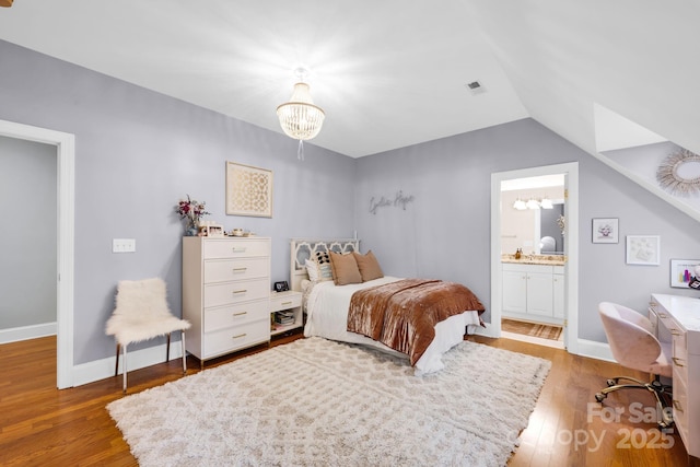 bedroom with a notable chandelier, visible vents, wood finished floors, ensuite bathroom, and vaulted ceiling