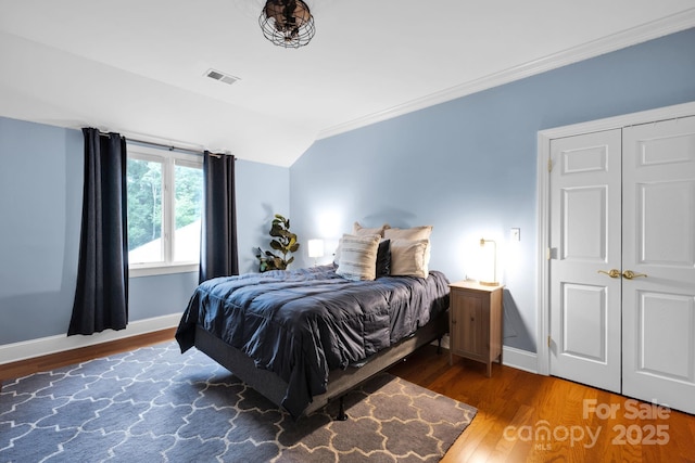 bedroom with baseboards, vaulted ceiling, wood finished floors, and visible vents
