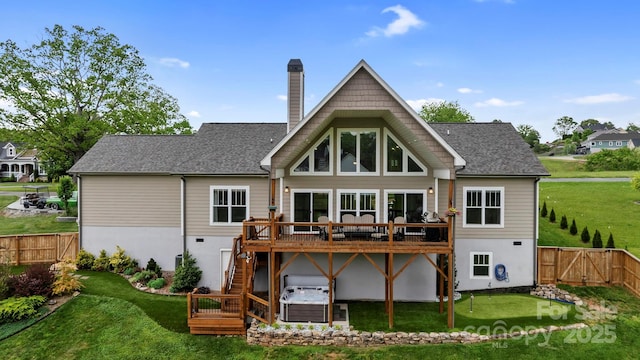 back of house featuring a wooden deck, fence, a chimney, a lawn, and a hot tub