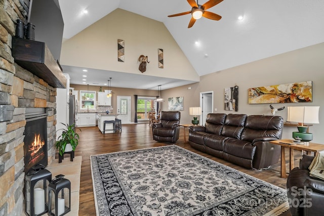 living area with dark wood-style flooring, a stone fireplace, high vaulted ceiling, recessed lighting, and a ceiling fan