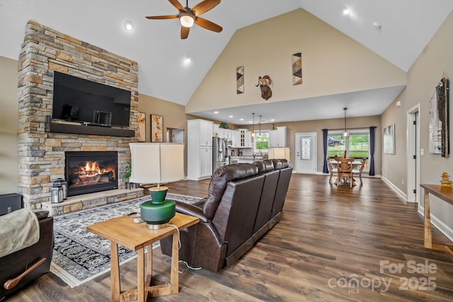 living area with high vaulted ceiling, ceiling fan, dark wood finished floors, and a stone fireplace